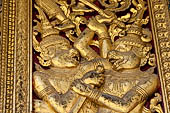 Wat Xieng Thong temple in Luang Prabang, Laos. Detail of a wooden door of the sim with gilded carvings on a red background. 